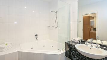 Un baño moderno con ducha de vidrio, una bañera amplia y una encimera de mármol con dos lavamanos.