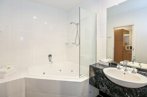 Un baño moderno con ducha de vidrio, una bañera amplia y una encimera de mármol con dos lavamanos.