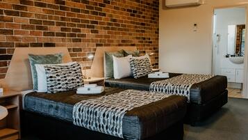 A hotel room with two beds, a brick wall, a white sink, and a mirror.