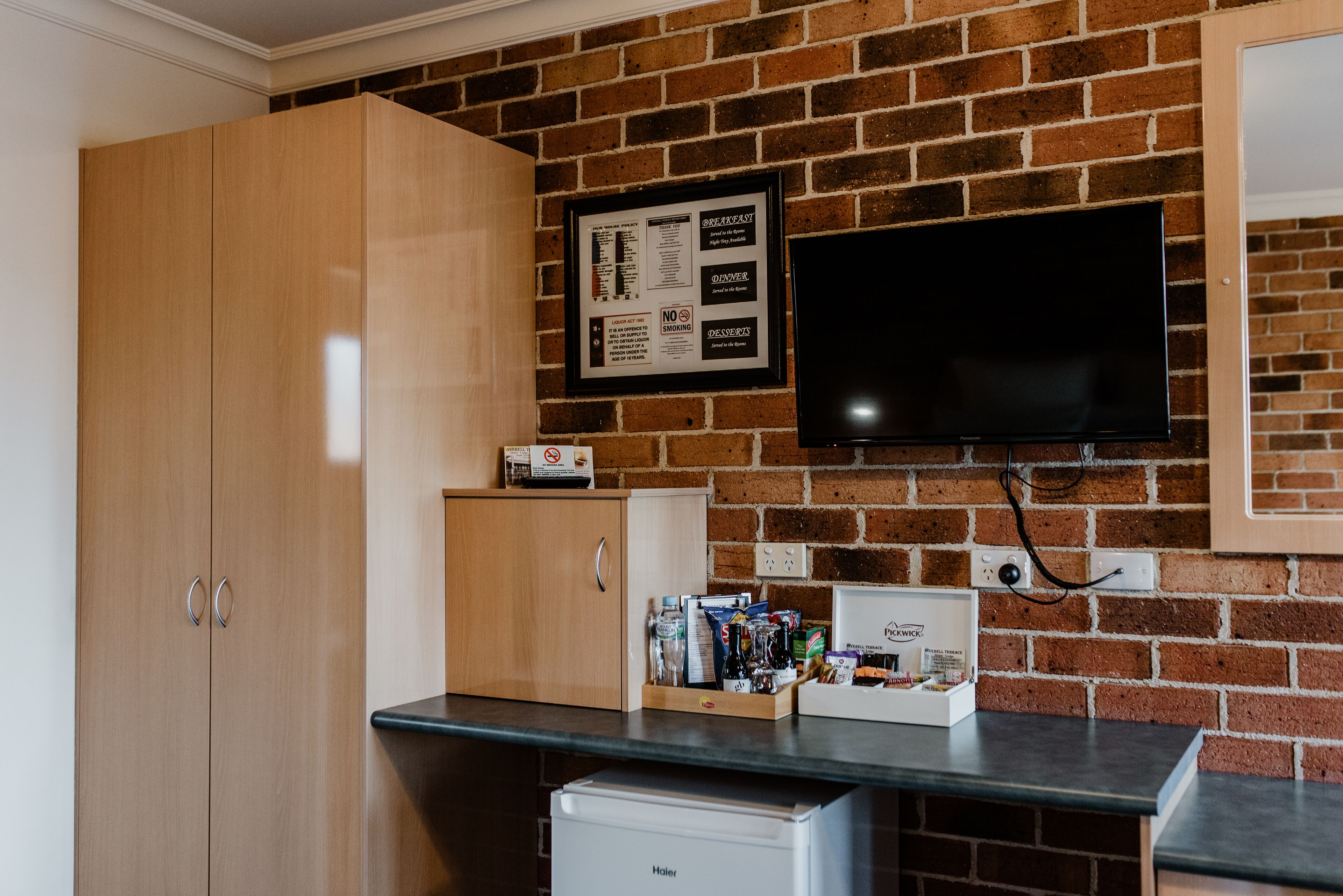 A kitchen with a brick wall, a wooden cabinet, a small refrigerator, and a framed menu on the wall.