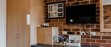 A kitchen with a brick wall, a wooden cabinet, a small refrigerator, and a framed menu on the wall.