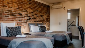 A hotel room with two beds, a brick wall, and a door leading to a bathroom. - Inverell Terrace Motor Lodge (Inverell)