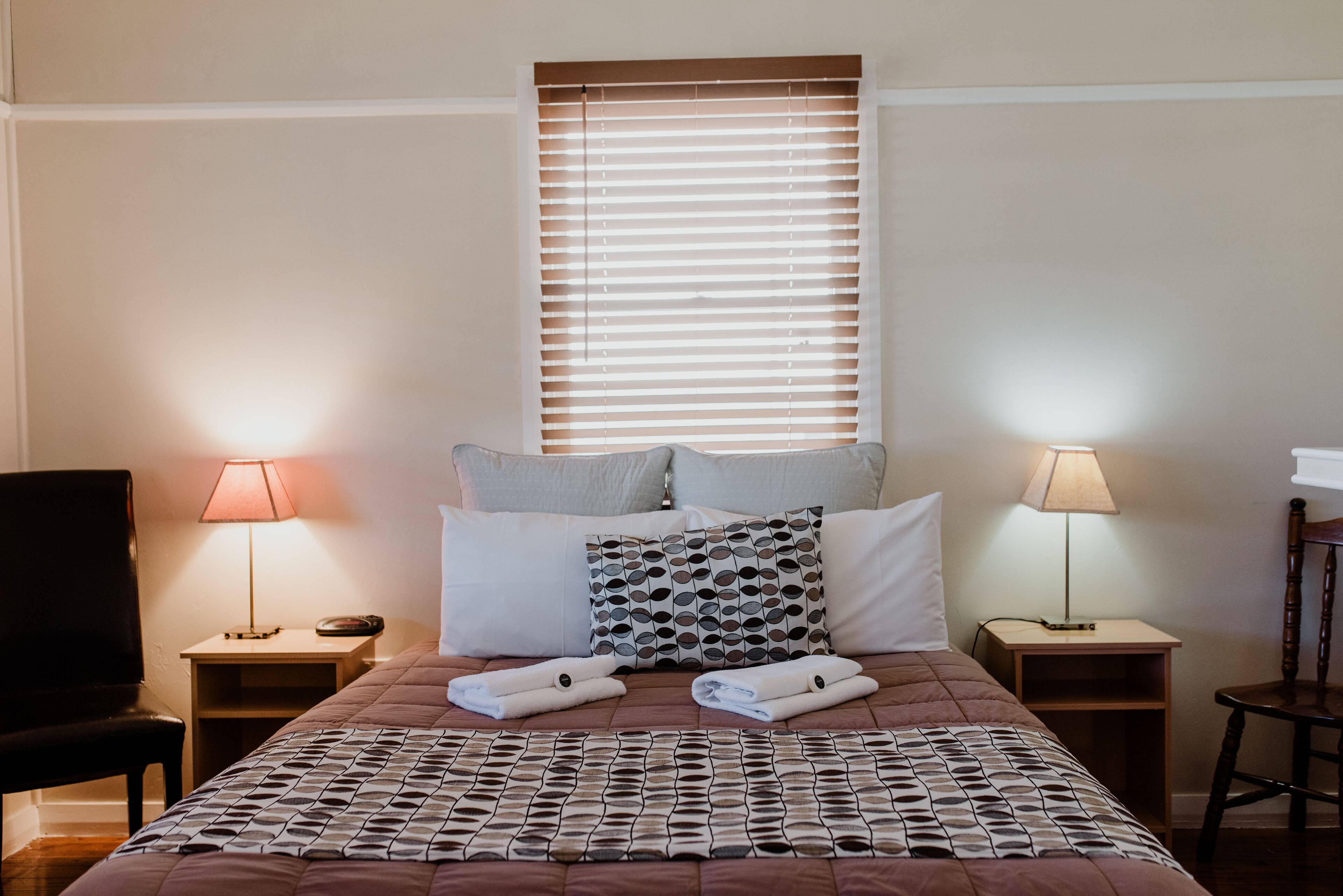 Una cama bien hecha con una colcha estampada, dos lámparas de noche y una ventana con persianas.