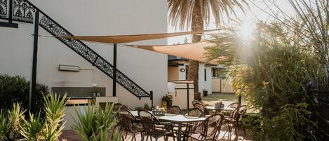 Un patio al aire libre con una mesa y sillas, rodeado de plantas en macetas y una palmera.