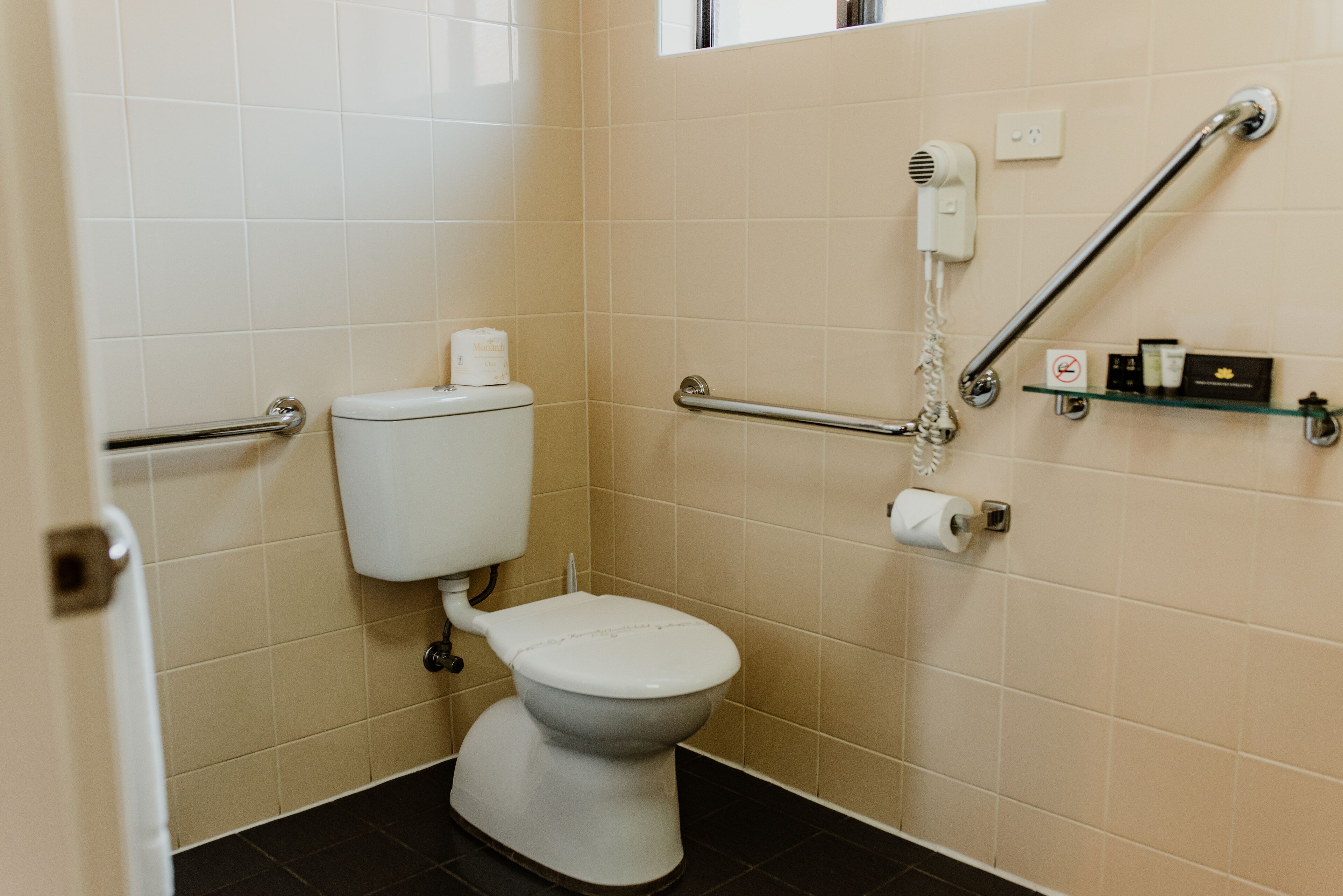 Ein Badezimmer mit Toilette, Haltegriffen, einem Föhn und einem Ablagefach für Pflegeprodukte.