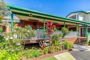A house with a covered porch, wooden deck, and a garden with various plants. - Maleny Hotel (Maleny)