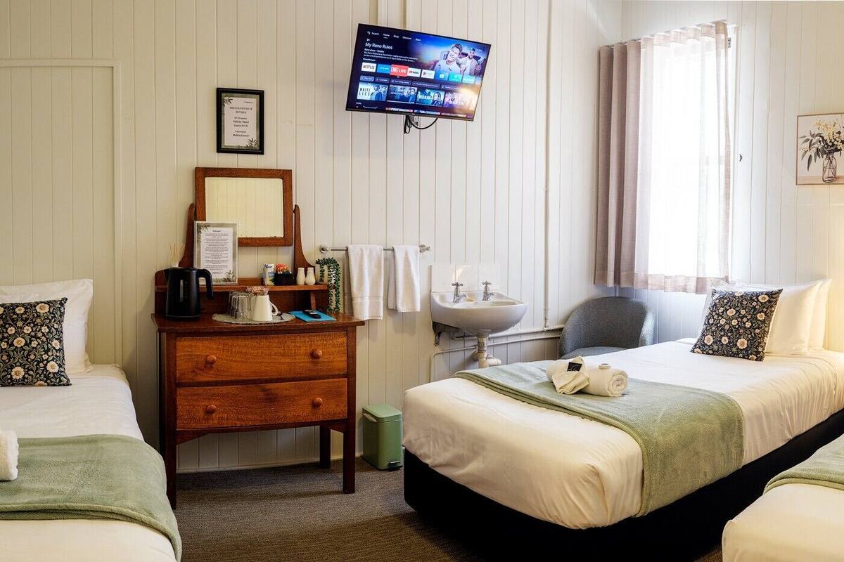 A hotel room with two beds, a wooden dresser, a TV, a sink, and framed artwork on the walls.