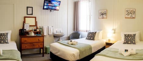 Ein Hotelzimmer mit zwei Betten, einer Holzkommode, einem Fernseher, einem Waschbecken und gerahmten Bildern an den Wänden.