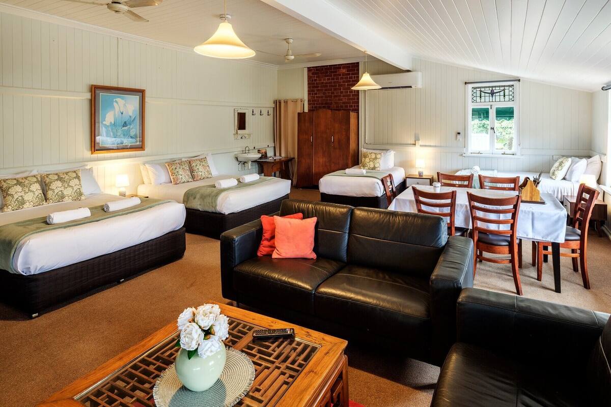A hotel room with a bed, two sofas, a dining table with chairs, a coffee table, and a vase of flowers.