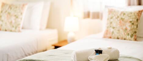 Habitación de hotel con dos camas, cada una con una colcha blanca y un cojín floral. Hay una manta verde sobre la cama en primer plano.