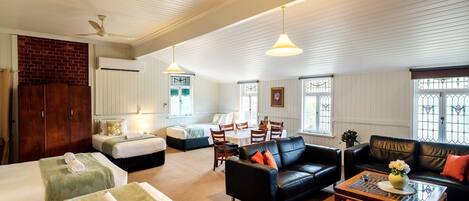 A hotel room with two beds, a sofa, a dining table, and a ceiling fan.