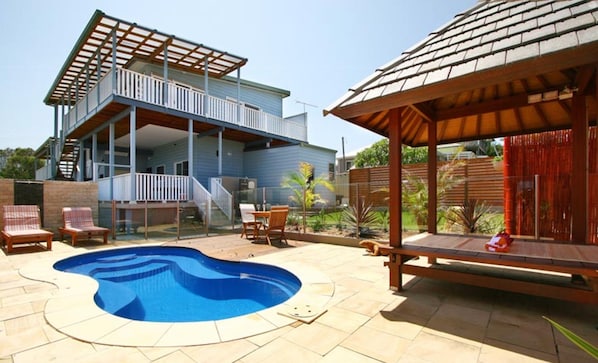Una casa de dos pisos con piscina en el patio trasero, un porche cubierto y un jardín cercado.
