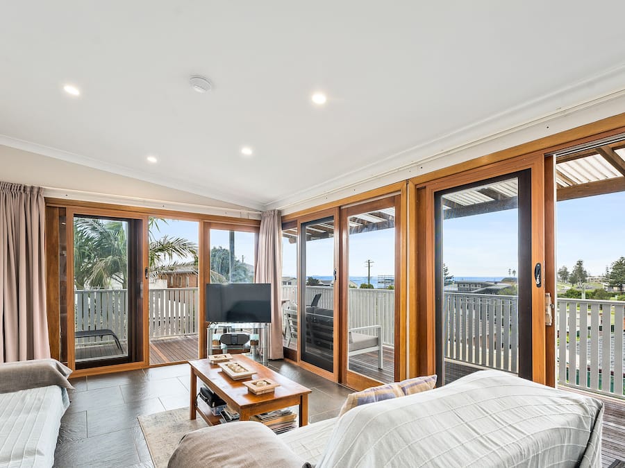 A spacious living area with a large sliding glass door leading to an outdoor balcony, a flat-screen TV, and a wooden coffee table.