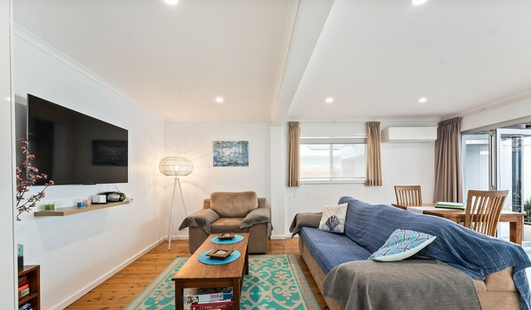 A modern living room with a flat-screen TV, a sofa, a coffee table, and a floor lamp. - Southview Boutique Guest House (Bulli)