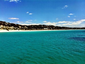 Une plage côtière aux eaux turquoise et limpides, bordée d’un rivage sablonneux.