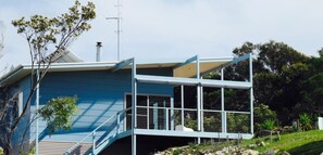 Une maison moderne avec une façade bleue, un balcon doté de rampes en métal et une cheminée.