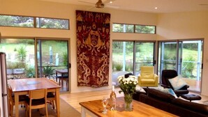 A spacious living area with a wooden dining table, a sofa, and a large window offering a view of the outdoors. - a Dune Escape (Emu Bay)