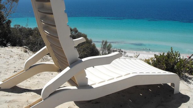 A white beach chair with a backrest, positioned on a sandy beach with a view of the ocean and clear blue sky. - a Dune Escape (Emu Bay)