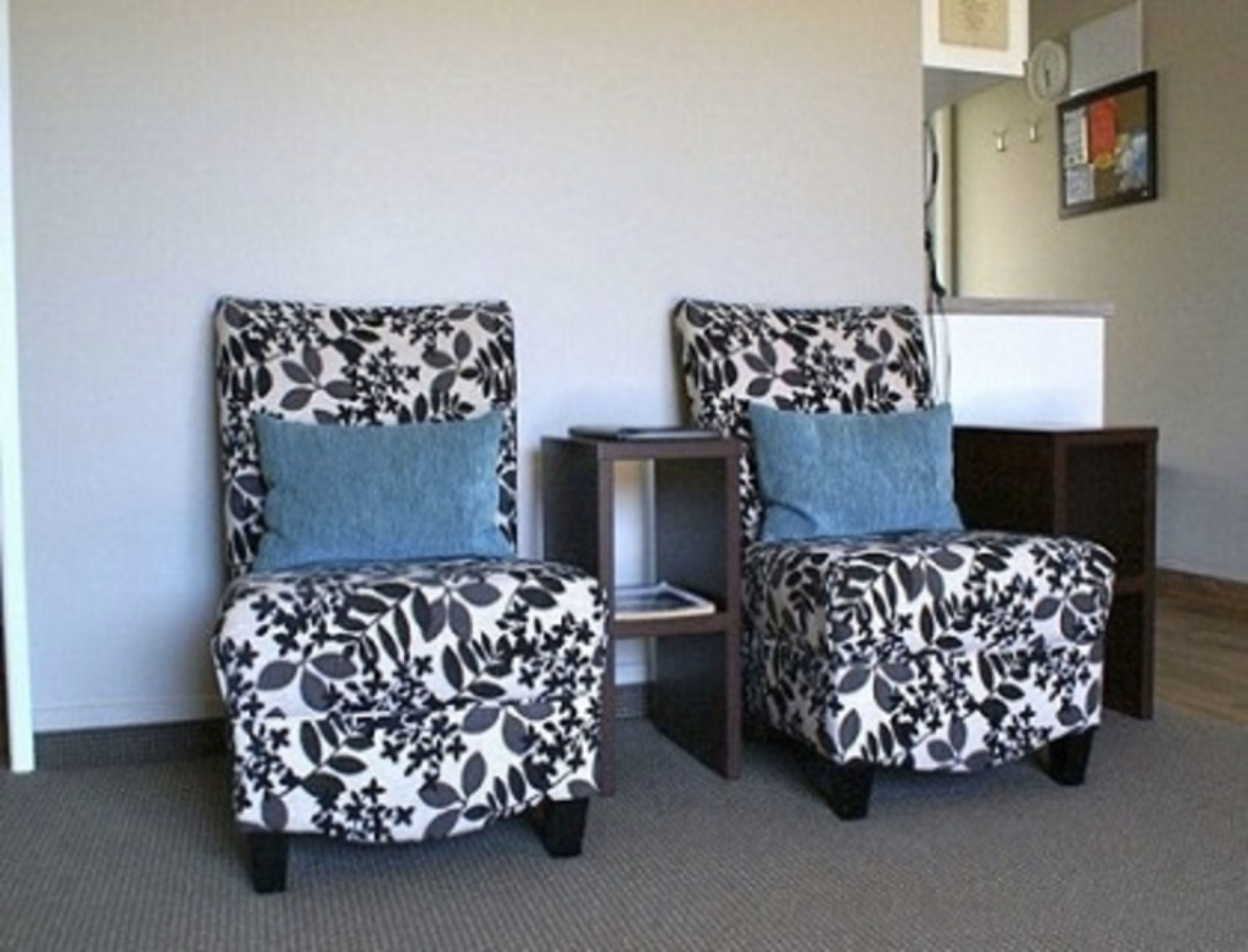 Two armchairs with floral upholstery and blue cushions, positioned against a wall with a small table and a clock.