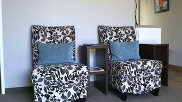 Dos sillones con tapicería floral y cojines azules, ubicados frente a una pared con una pequeña mesa y un reloj.
