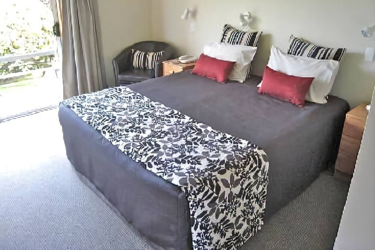 Een hotelkamer met een groot bed, een stoel, een nachtkastje en uitzicht op het buitenleven.