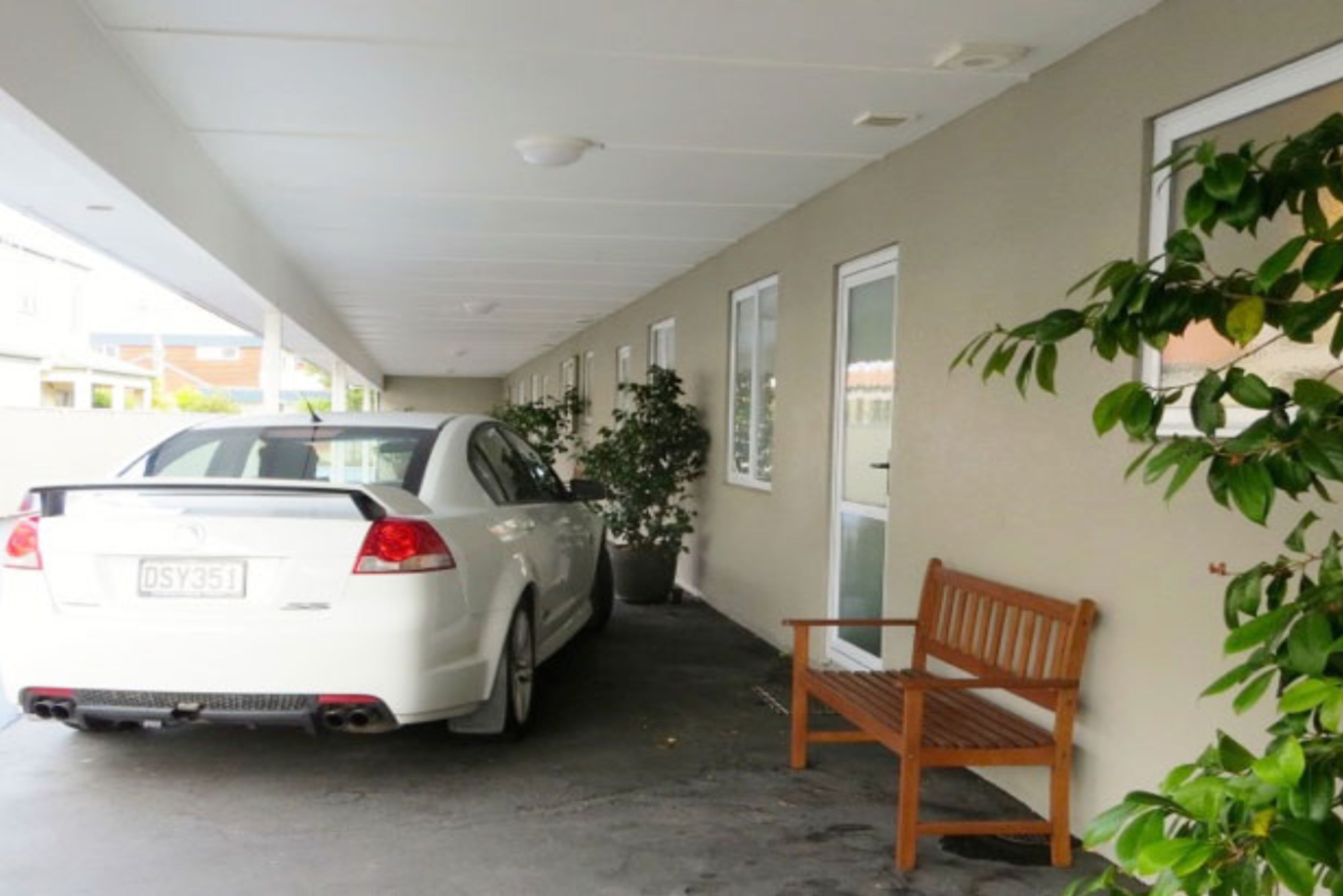 Un espace de stationnement couvert avec une voiture blanche, un banc et une plante en pot.