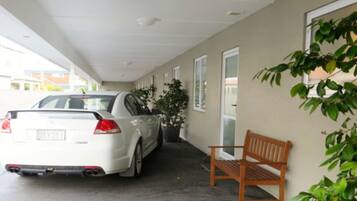 Un espace de stationnement couvert avec une voiture blanche, un banc et une plante en pot.