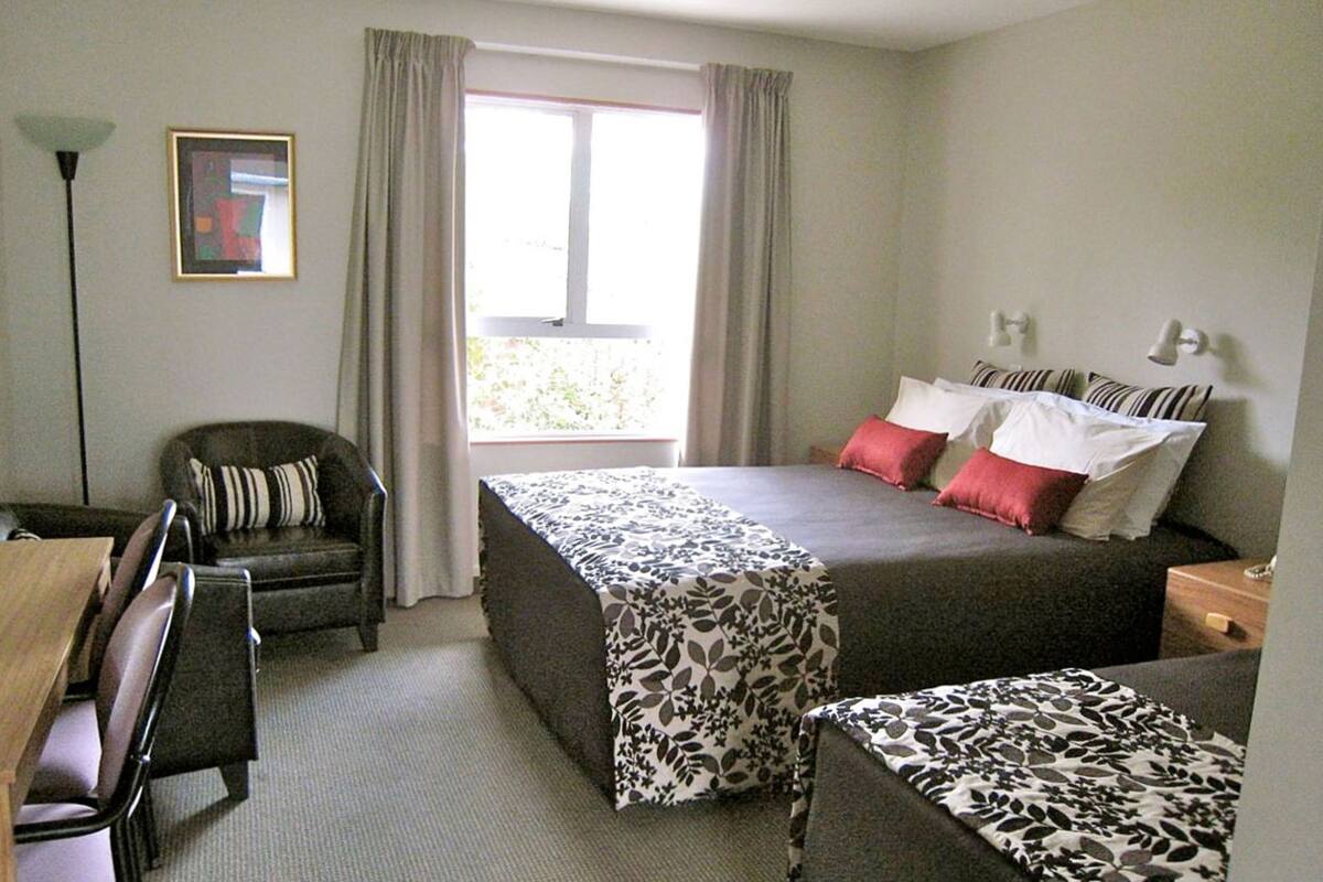 Een hotelkamer met een bed, een bureau, een stoel en een raam met gordijnen.