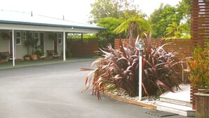 A modern building with a covered patio area, a concrete driveway, and a landscaped garden with large plants and a palm tree.