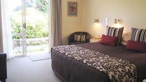 A hotel room with a large bed, a chair, a desk with a telephone, and a door leading to a balcony.