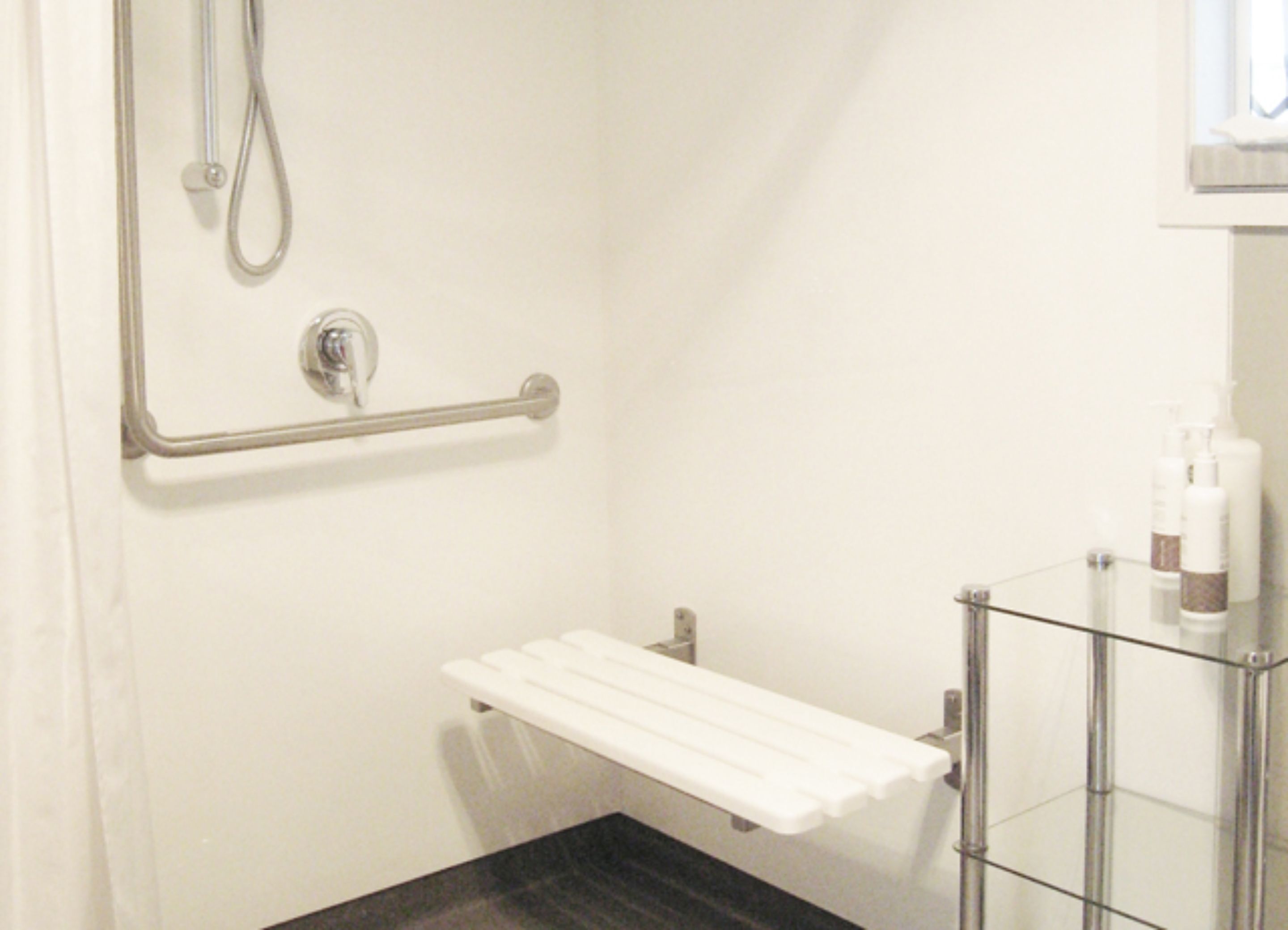 A bathroom with a shower, grab bar, and a glass shelf with toiletries.