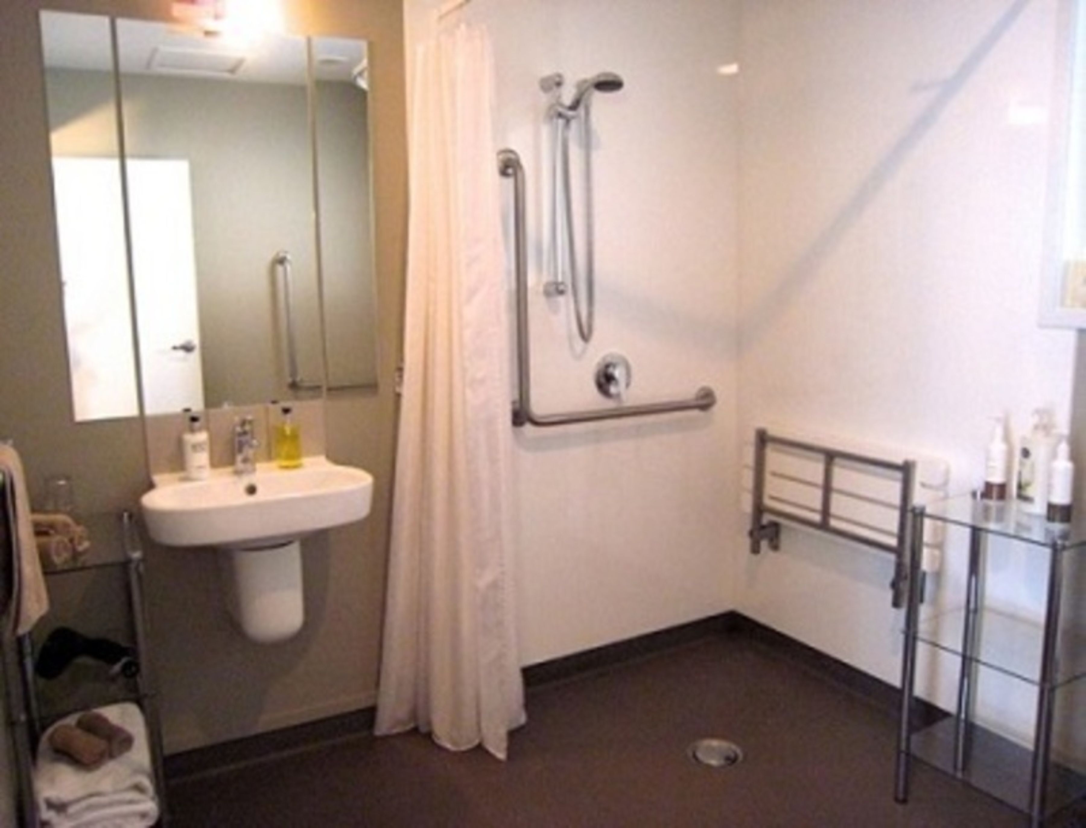 A bathroom with a sink, mirror, shower, and a glass partition.
