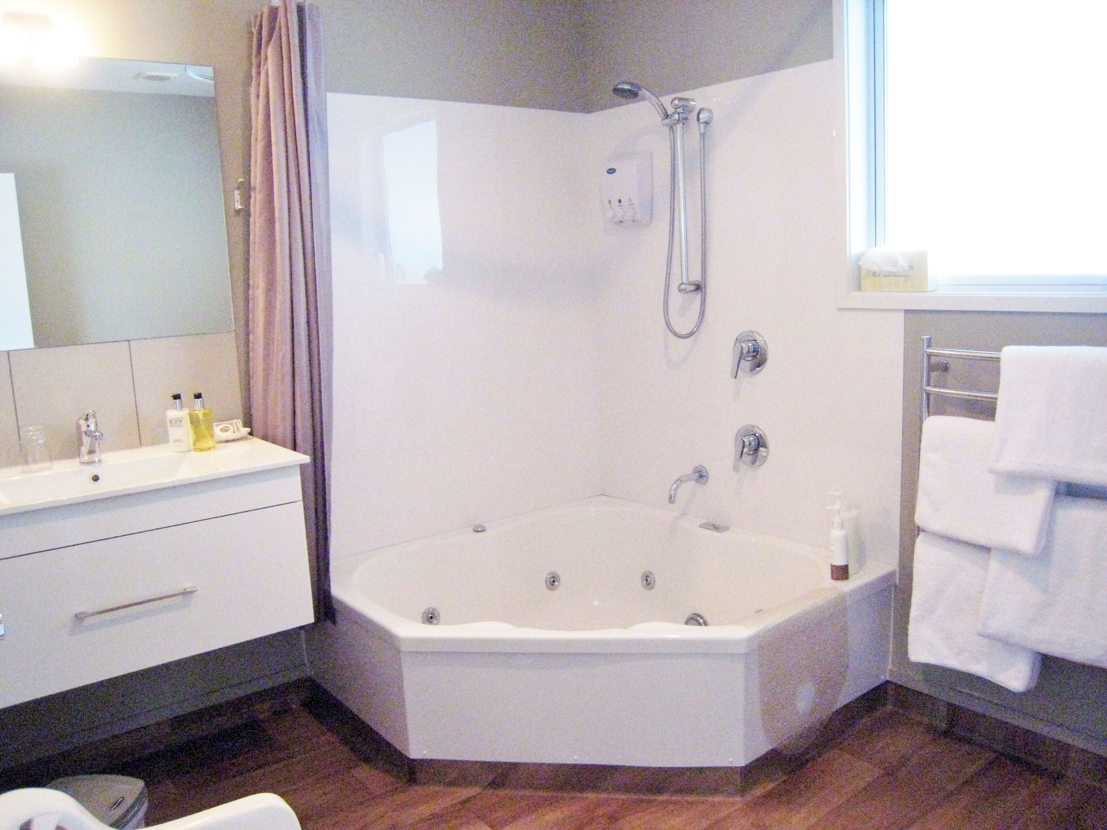 A corner bathroom with a white bathtub, a shower, a sink with toiletries, and a mirror.