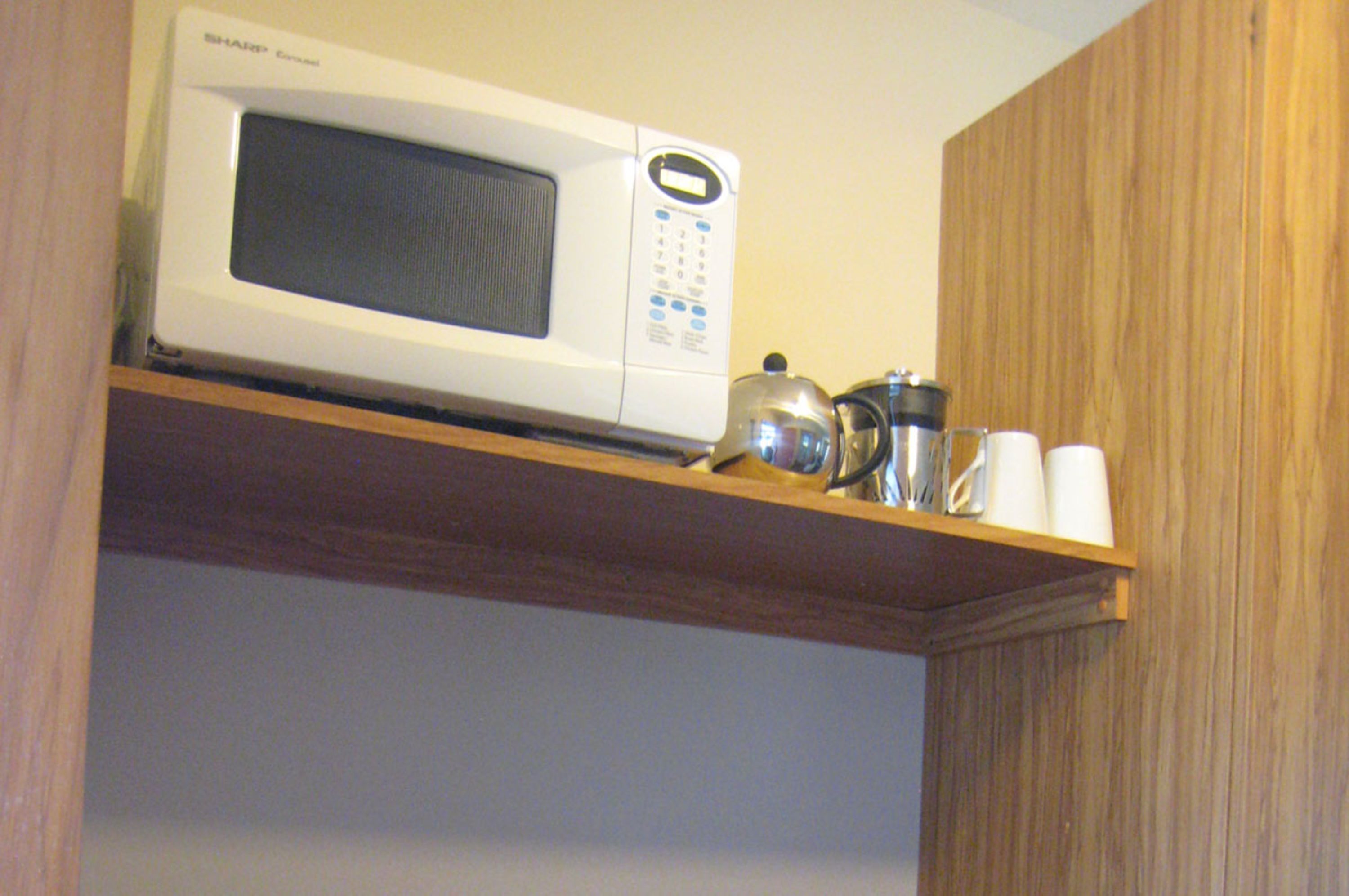A microwave on a wooden shelf in a kitchen.