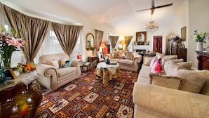 A spacious living room with a large patterned rug, a ceiling fan, and a chandelier. - Katoomba Manor (Katoomba)
