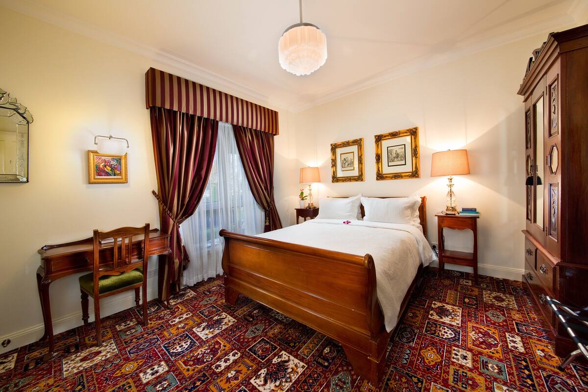 A traditional bedroom with a wooden bed, a desk, and a patterned carpet.