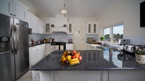 A modern kitchen with white cabinetry, a granite countertop, and a fruit bowl. - Katoomba Manor (Katoomba)