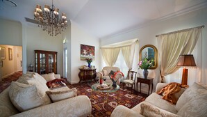 A spacious living room with a large chandelier, comfortable seating, a coffee table with fruit, and a decorative mirror. - Katoomba Manor (Katoomba)