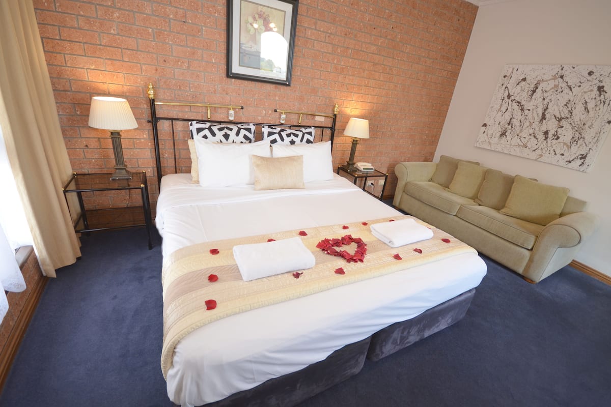 A hotel room with a bed, two bedside tables, a sofa, a brick wall, and a painting.