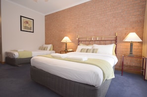 Habitación de hotel con dos camas, una pared de ladrillo y dos lámparas de noche.