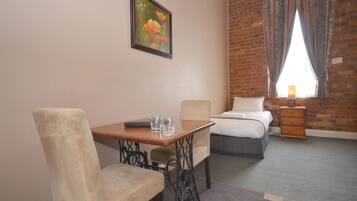A hotel room with a brick wall, a bed, a desk with a chair, and a painting on the wall.