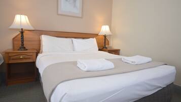 A neatly made bed with white linens and a beige throw blanket, flanked by two bedside tables with lamps, in a hotel room.