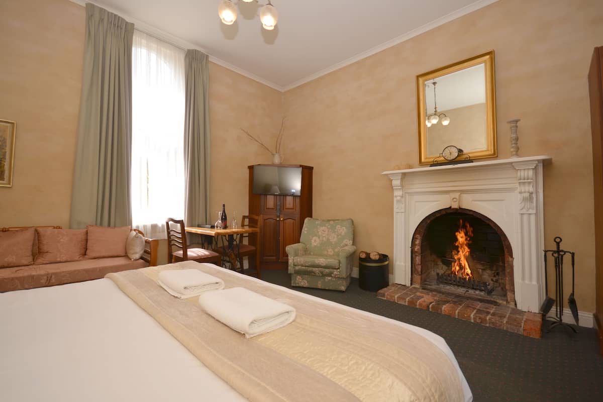 A hotel room with a large bed, a fireplace, a dining area, and a television.