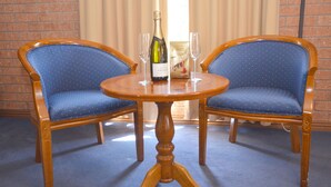 Dos sillones tapizados en azul con estructura de madera y una mesa de madera con una botella de champán y dos copas.