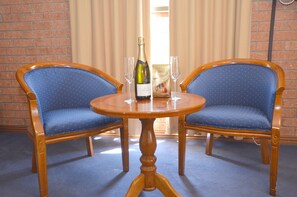 Two blue upholstered chairs with wooden frames and a wooden table with a bottle of champagne and two glasses.