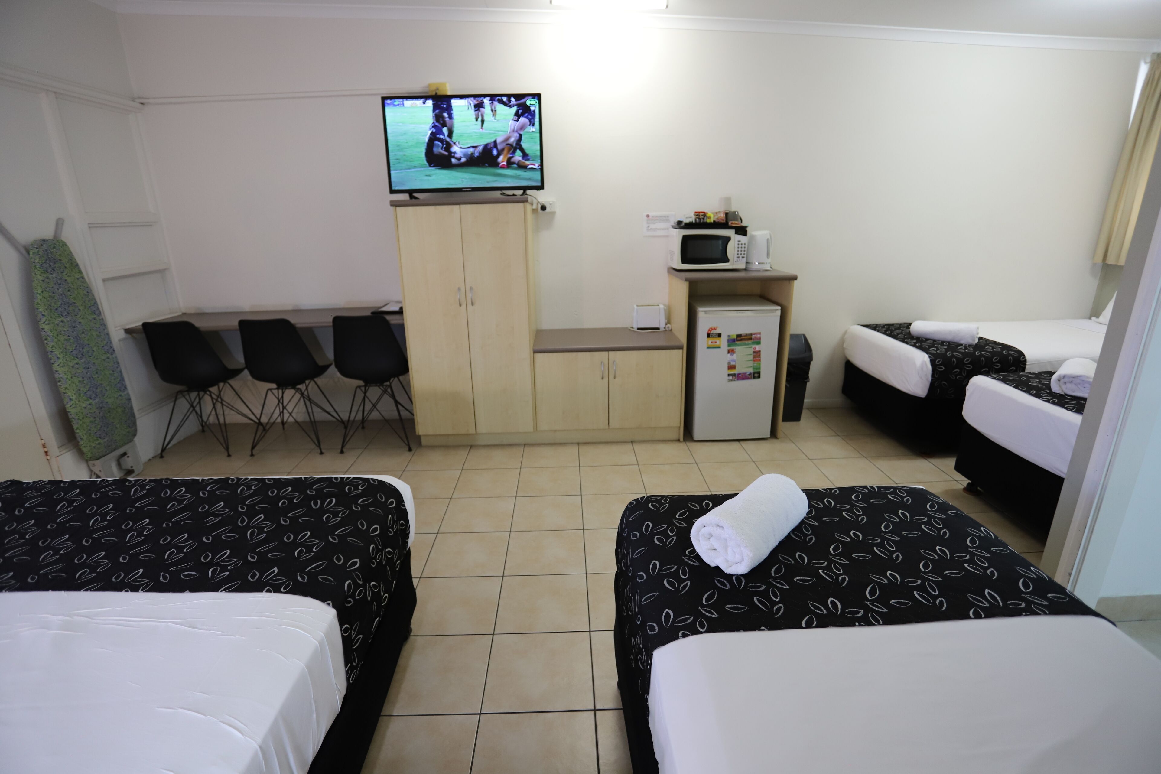 A hotel room with two beds, a TV, a small kitchenette, and a seating area with chairs.