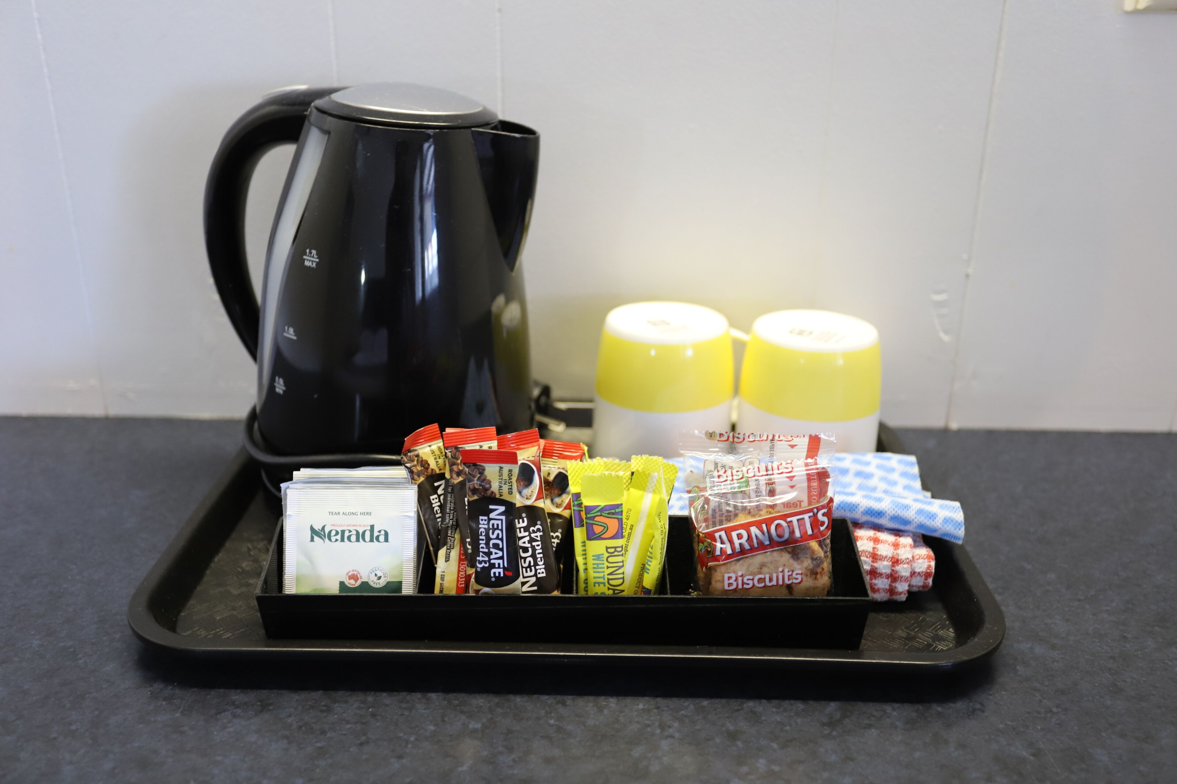 A tray with a black coffee maker, two yellow bottles, and various packaged snacks.
