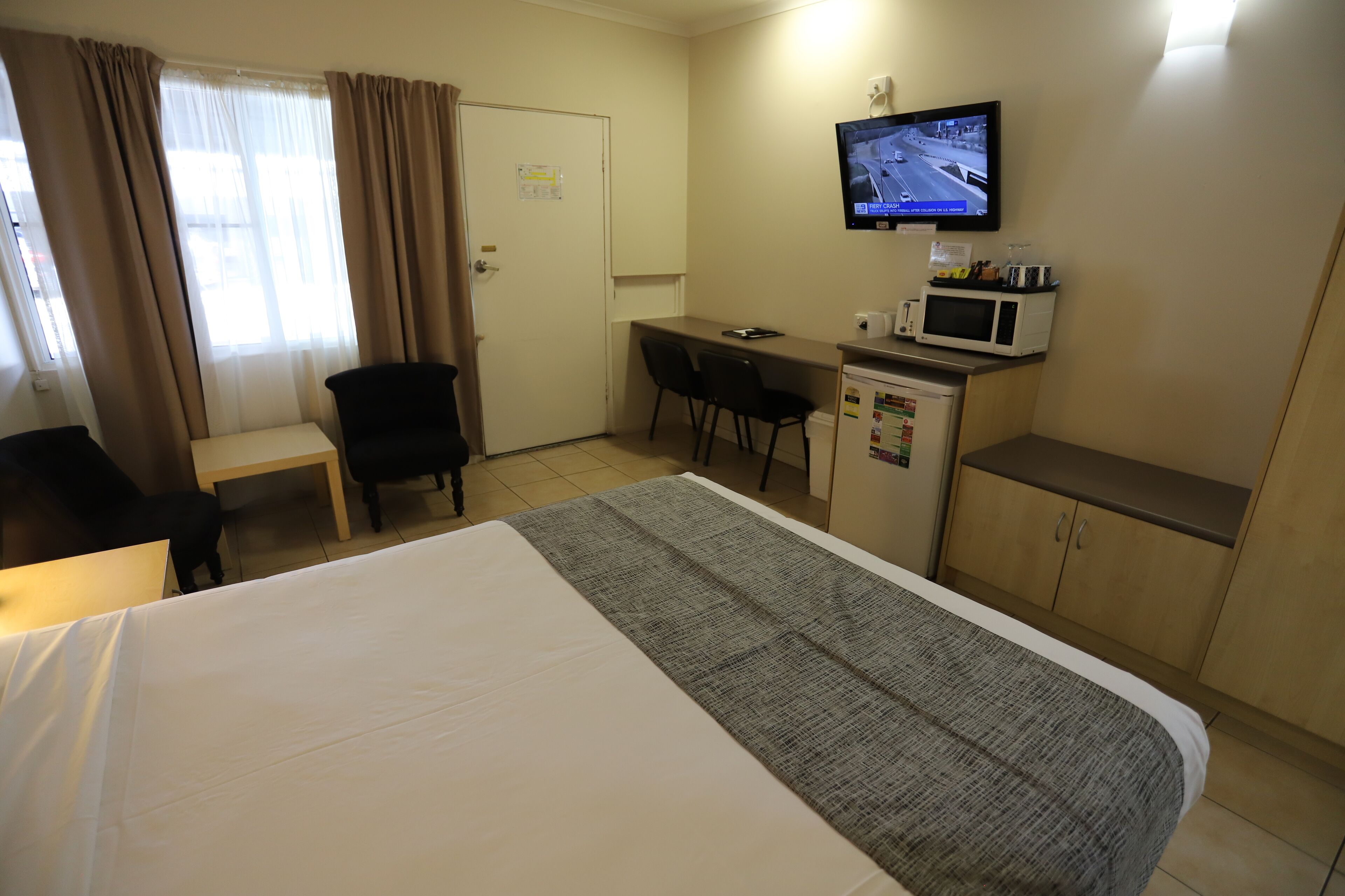A hotel room with a bed, a desk with a chair, a television mounted on the wall, and a microwave on the desk.