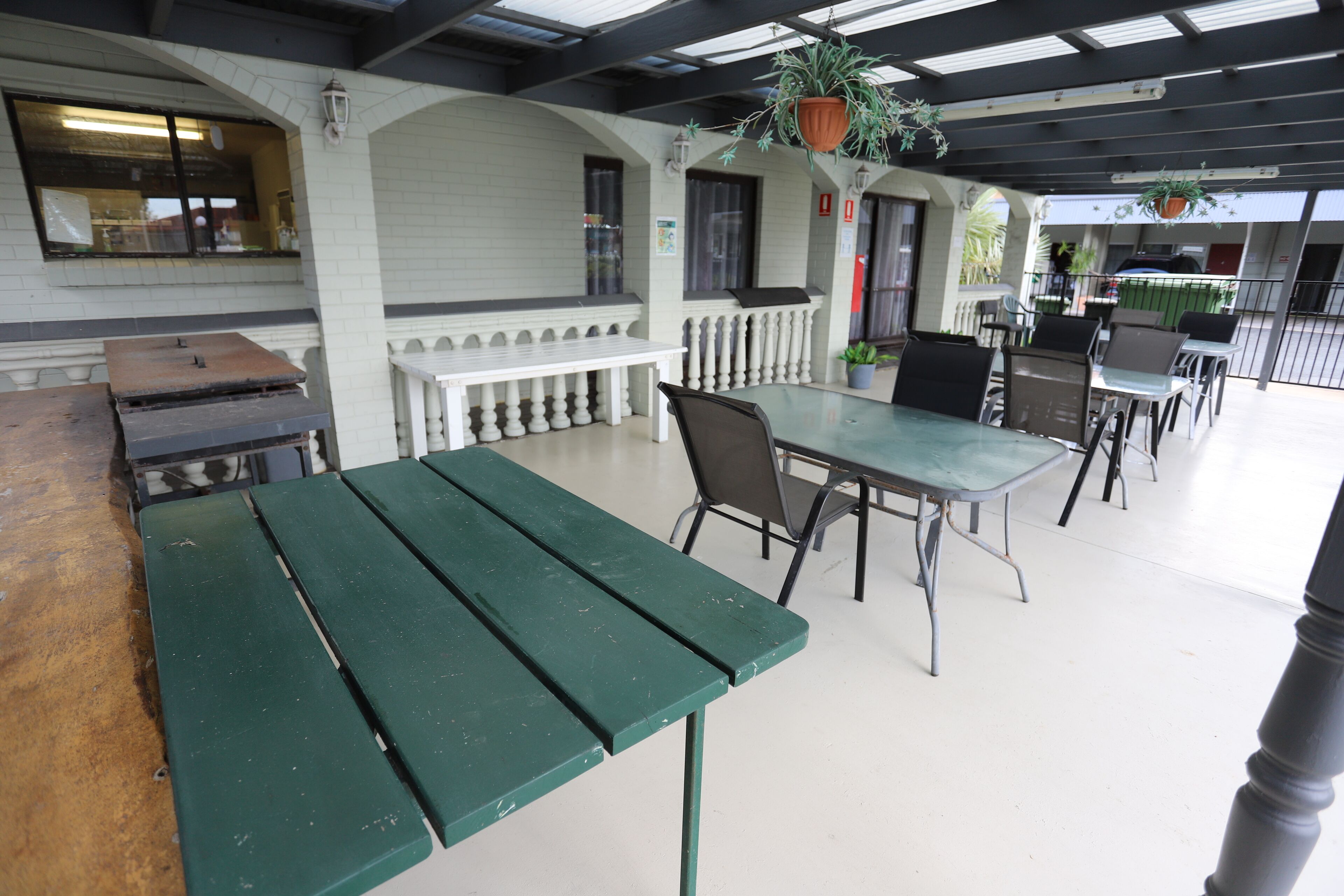 Een terras buiten met een groene tafel en stoelen, witte leuningen en hangplanten.
