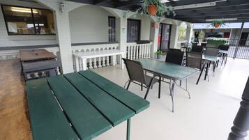 Een terras buiten met een groene tafel en stoelen, witte leuningen en hangplanten.